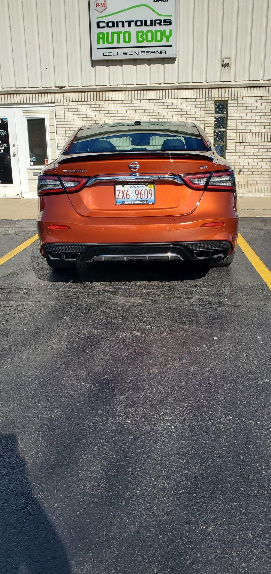 A red car is parked in a parking lot in front of a building.