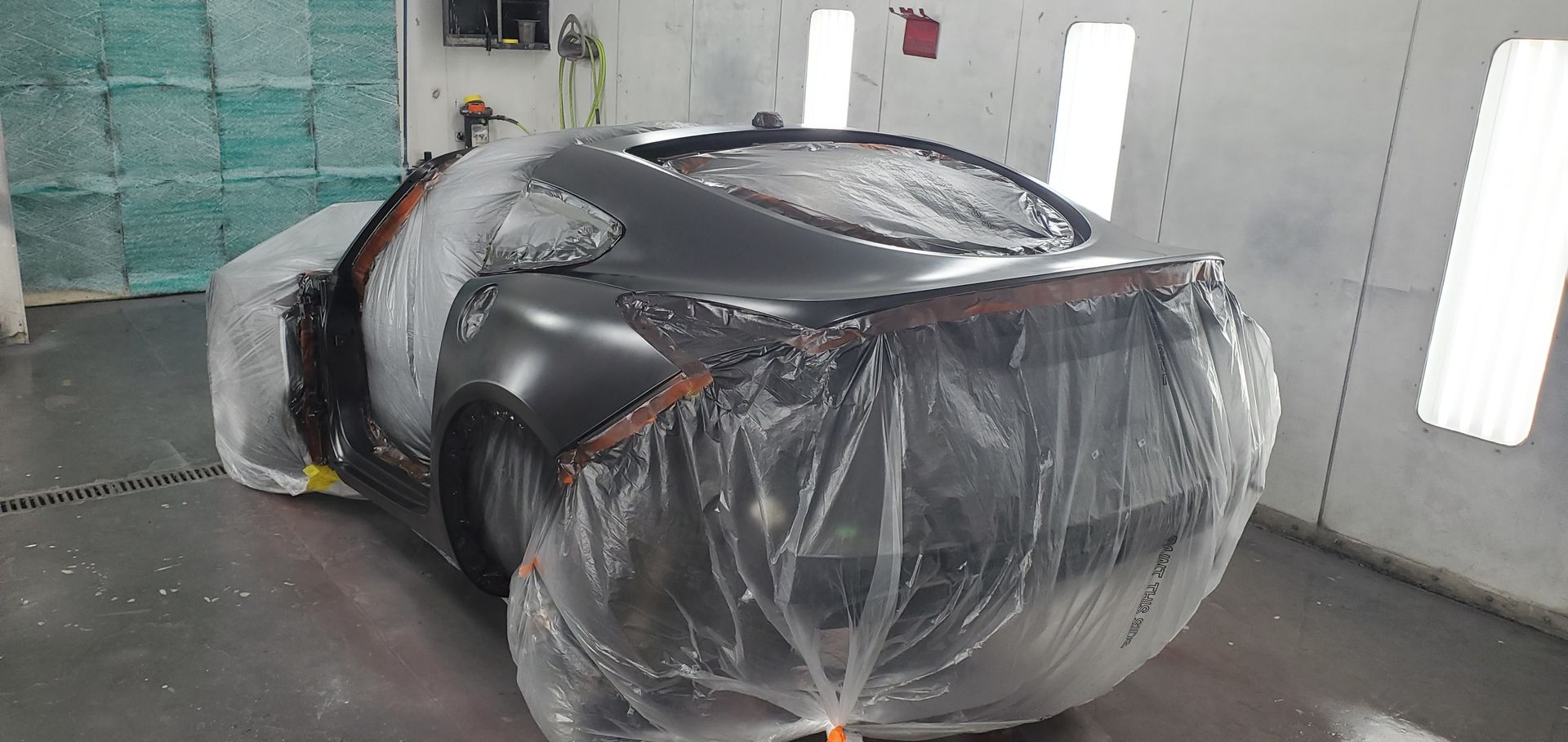A car is covered in plastic in a paint booth.