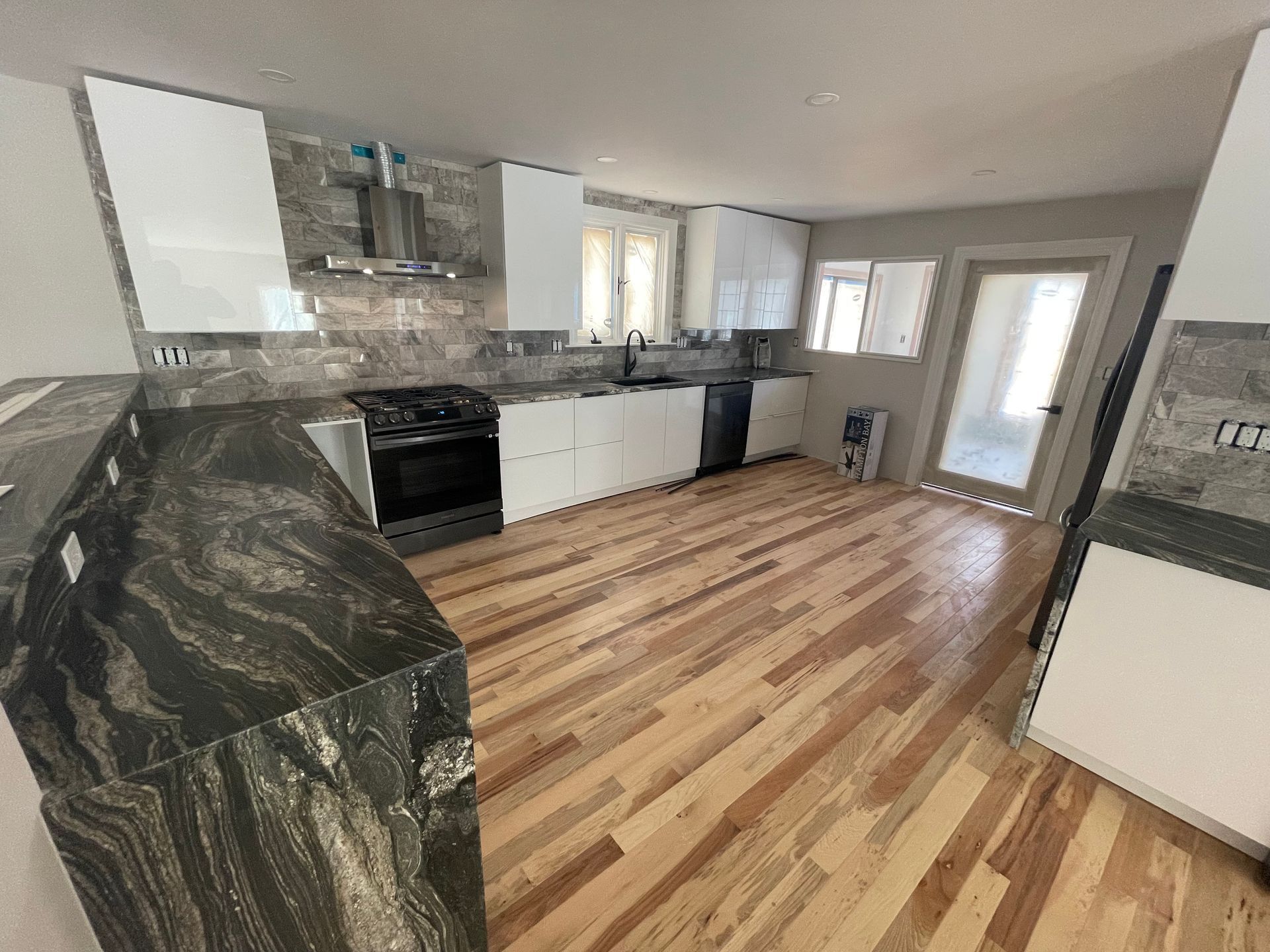 Modern kitchen with white cabinets, black granite countertops, stainless steel appliances, and wood flooring.