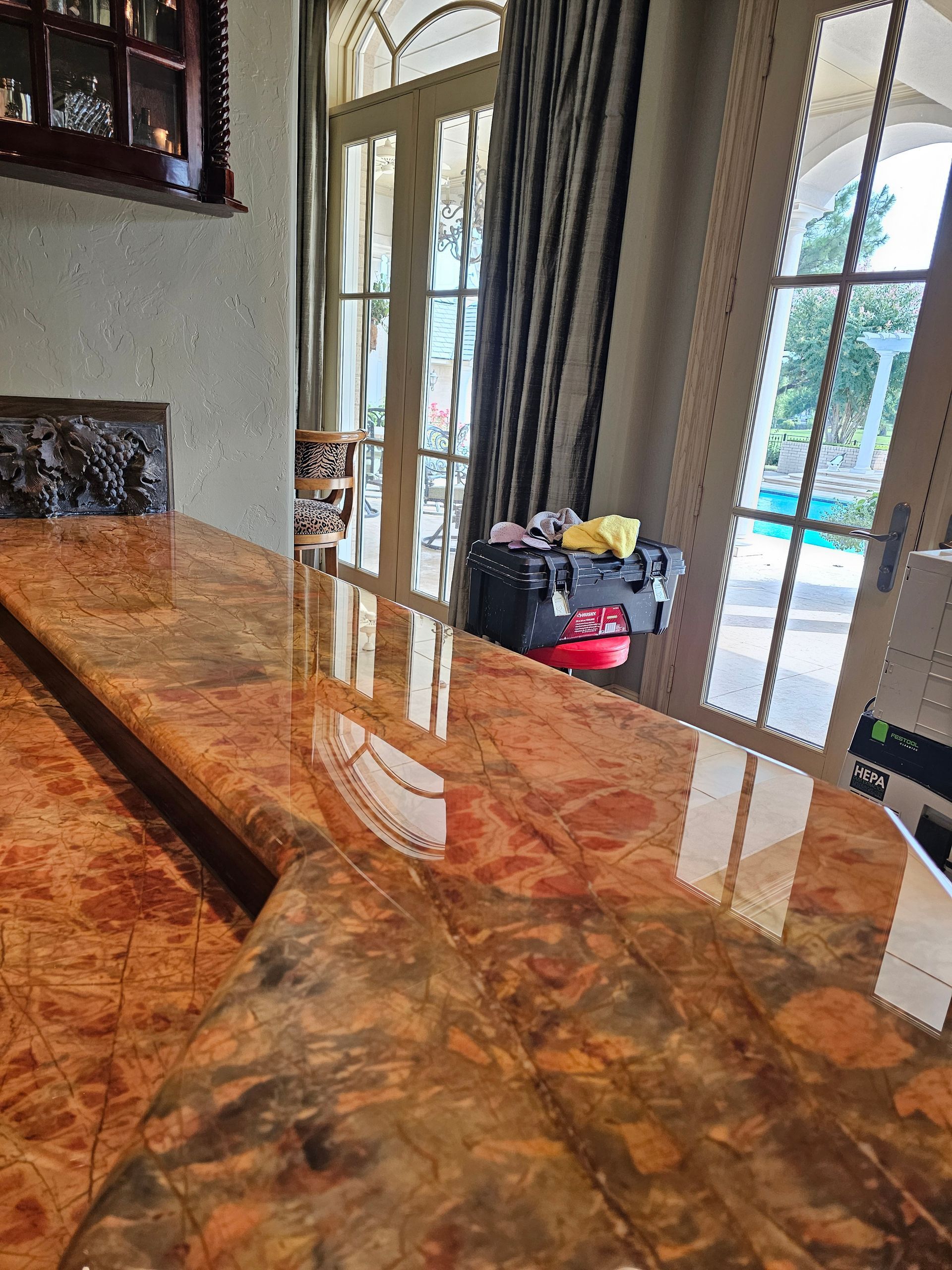 Polished, brown and orange marble countertop reflecting sunlight and the room's interior.