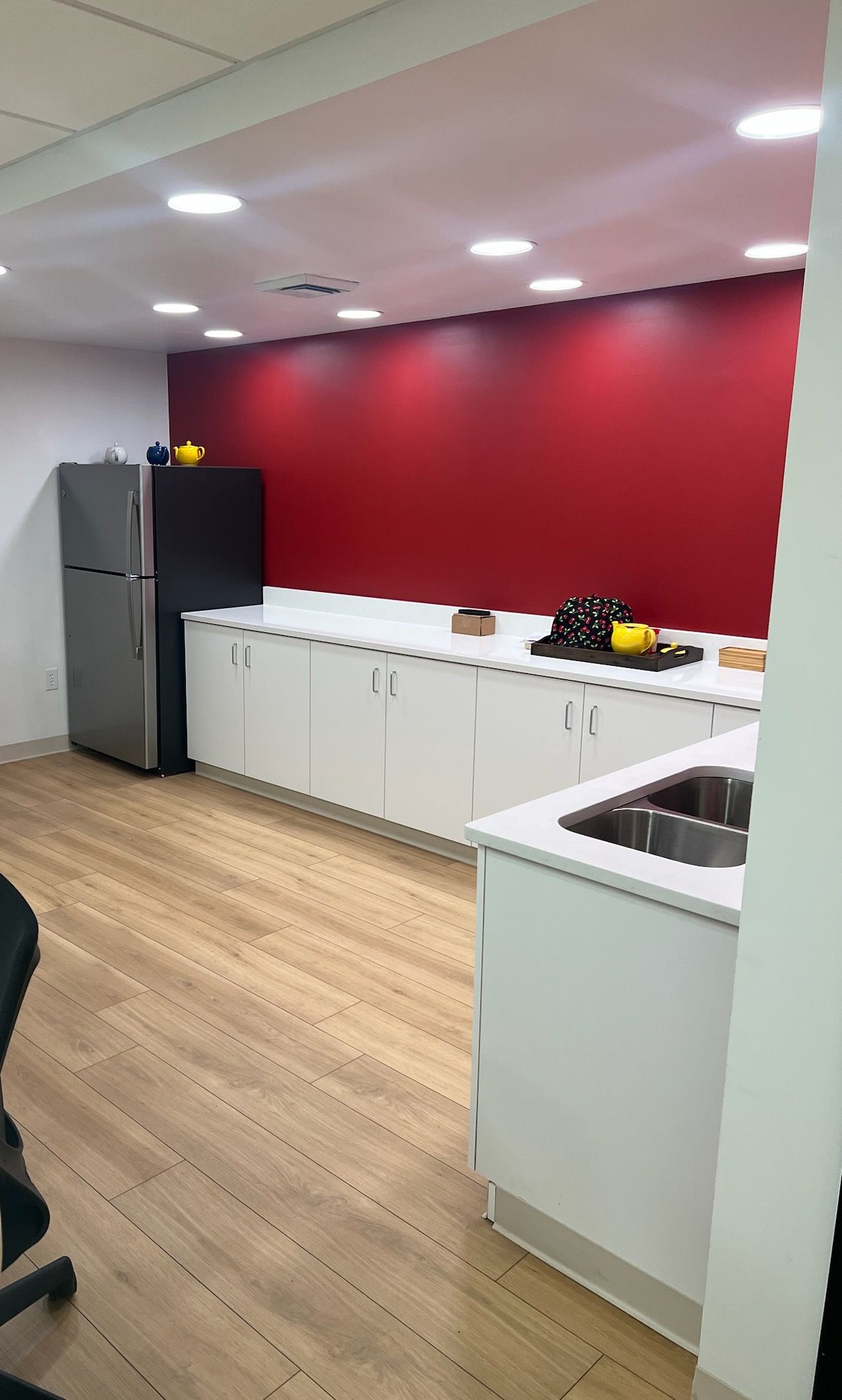 A kitchen with a refrigerator , sink , cabinets and a red wall.