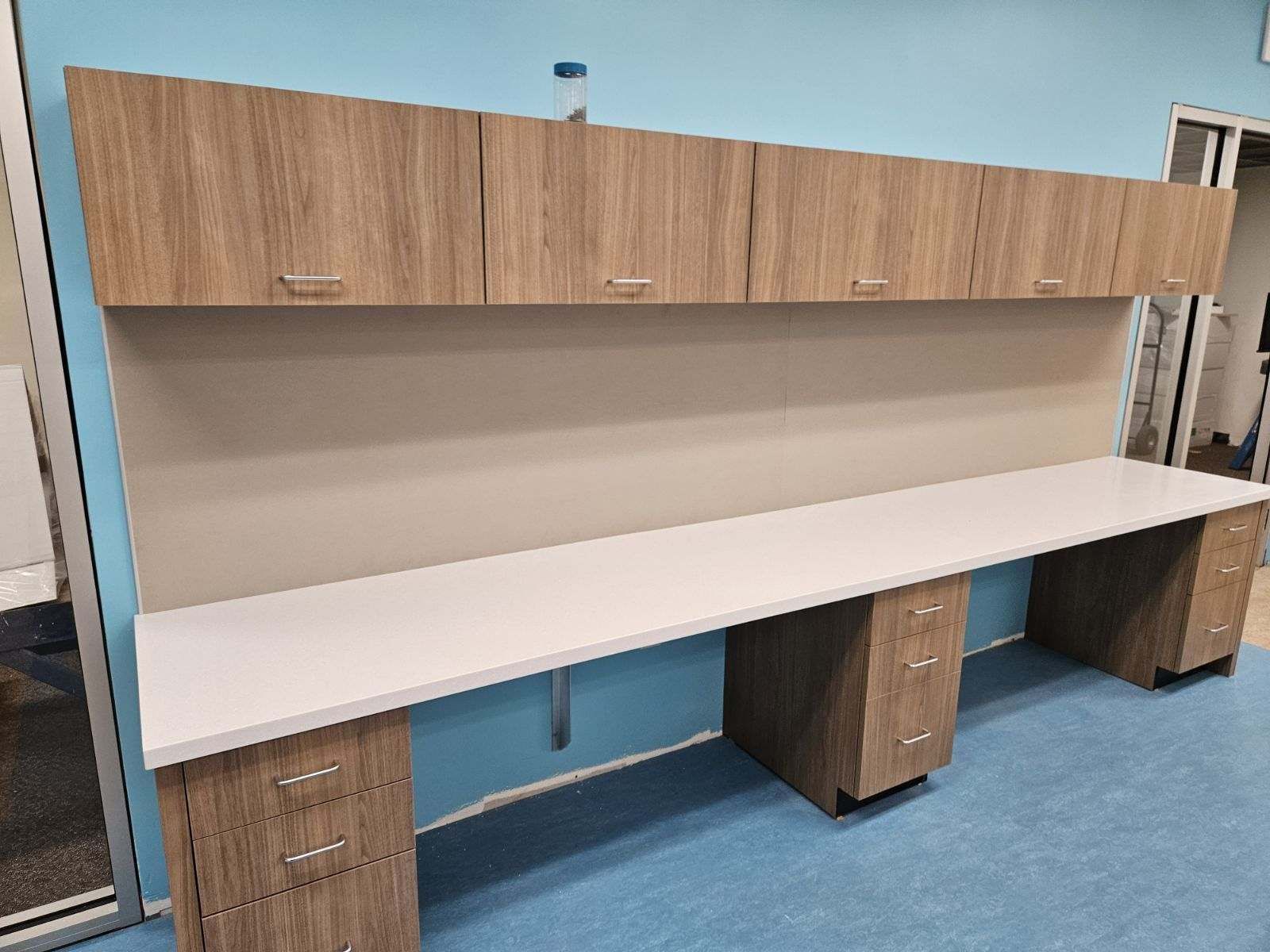 A long desk with drawers and cabinets in a room with a blue wall.