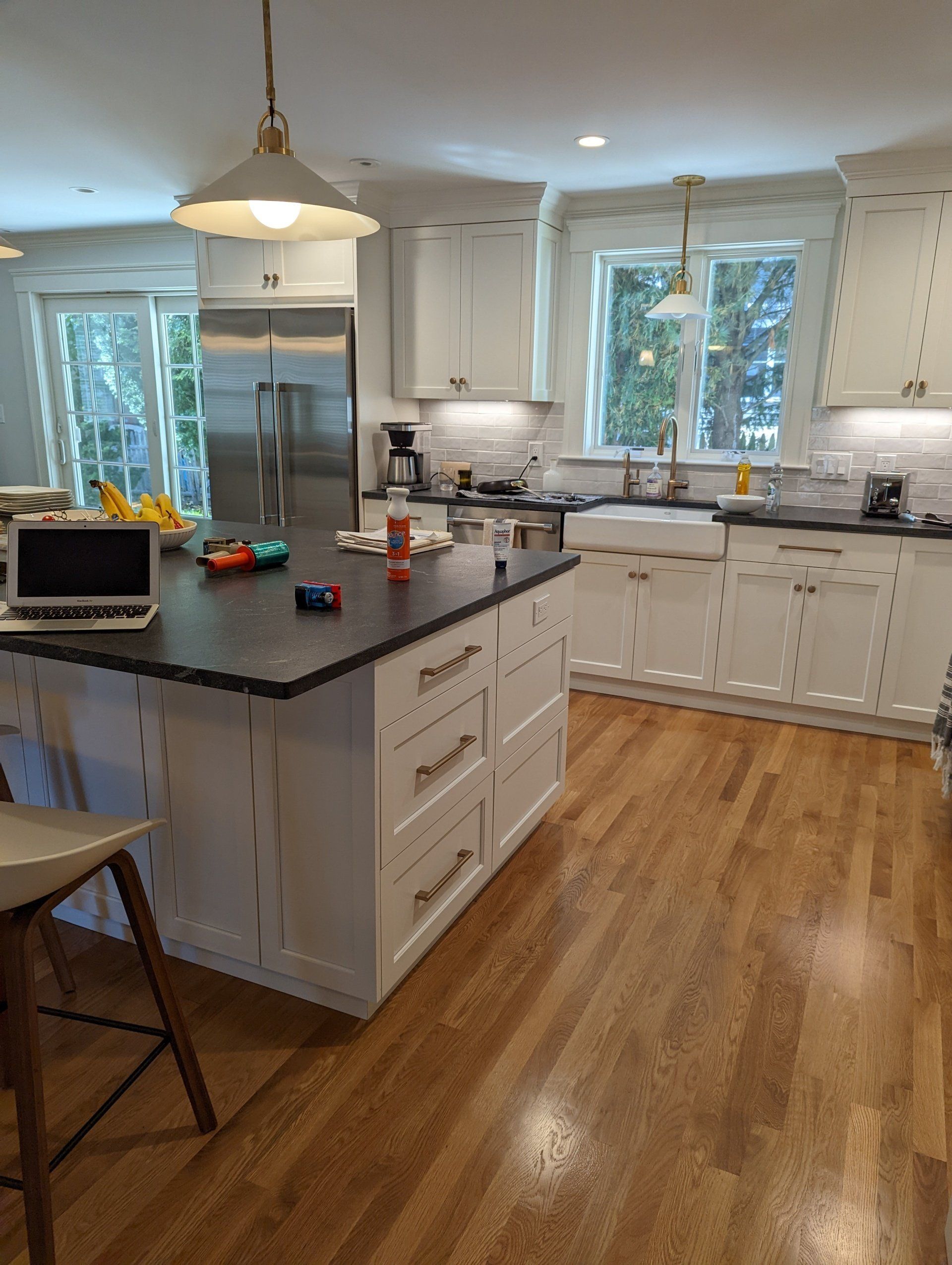 A kitchen with white cabinets and hardwood floors and a laptop on the counter.