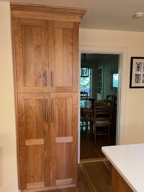 A wooden cabinet in a kitchen next to a door leading to a dining room.
