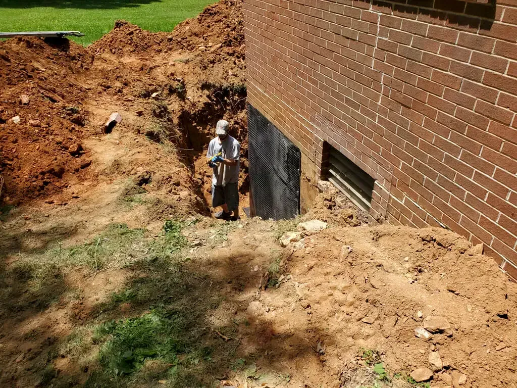 A man is digging a hole in the side of a brick building.