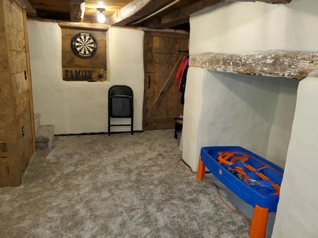 A basement with a dart board , chair , and toy table.