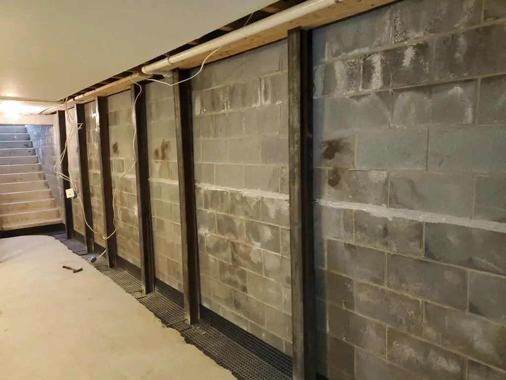 A row of brick walls in a basement with stairs in the background.