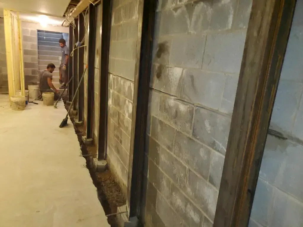 A group of men are working on a brick wall in a basement.