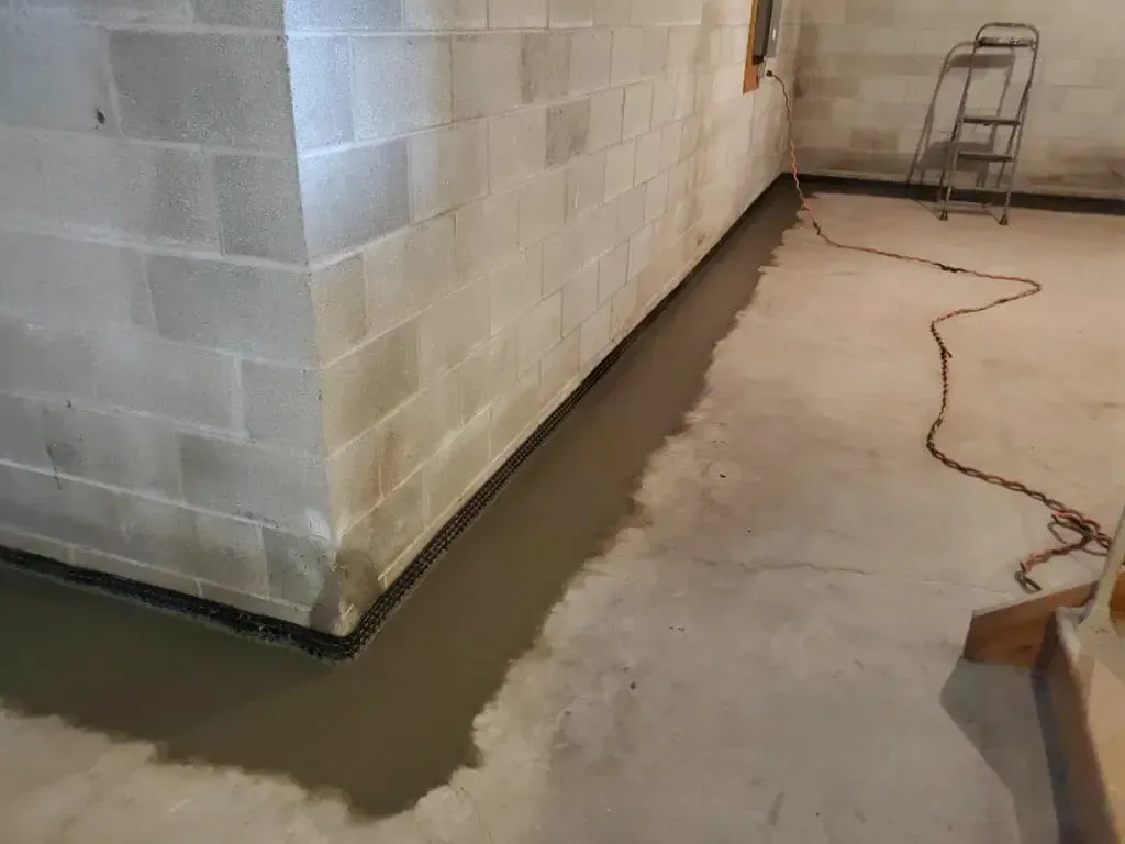 A person is laying concrete in a basement next to a brick wall.