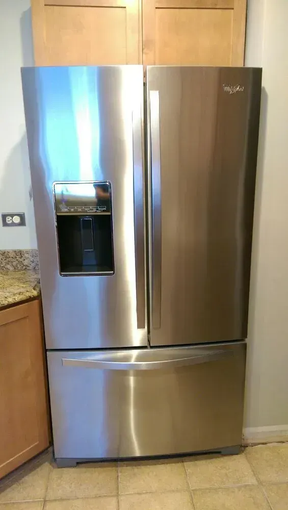 Stainless steel Whirlpool refrigerator with ice/water dispenser, in a kitchen setting.
