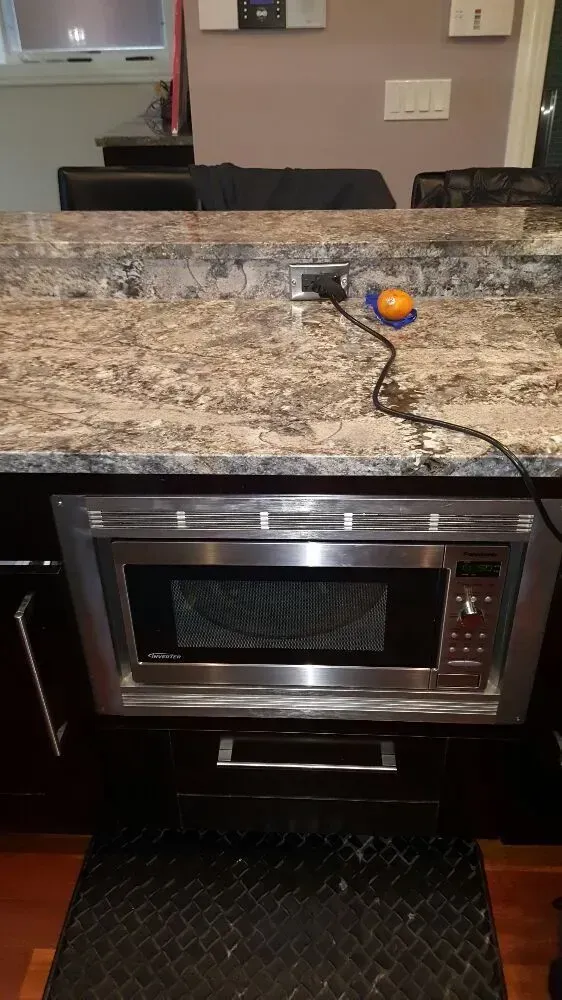 Microwave oven built into dark cabinets under a granite countertop with a power outlet above.