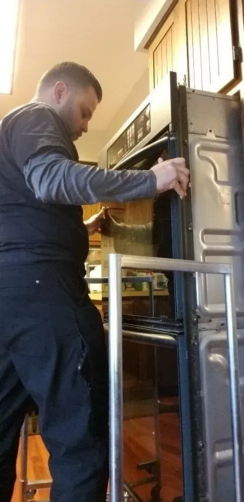 A person is removing an oven door in a kitchen, likely for repair.