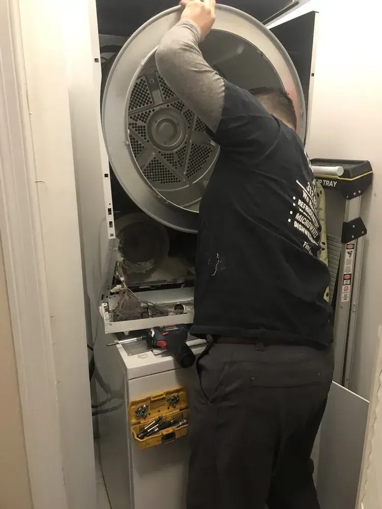 Man removing the drum from a white washing machine, in a utility closet.