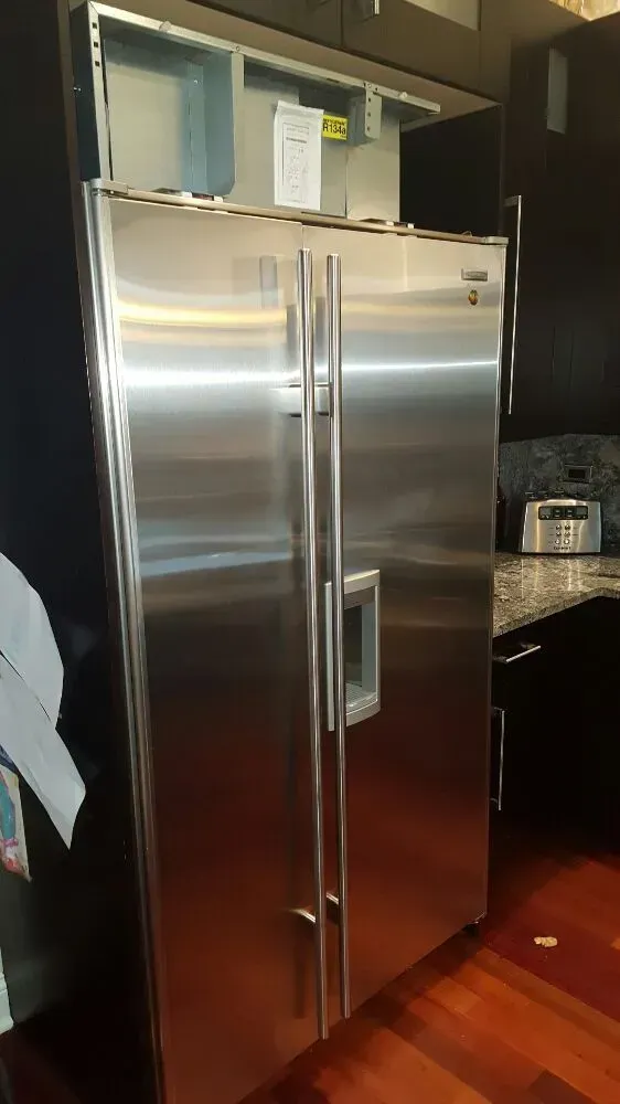 Stainless steel side-by-side refrigerator in a kitchen with dark cabinets and wood floors.