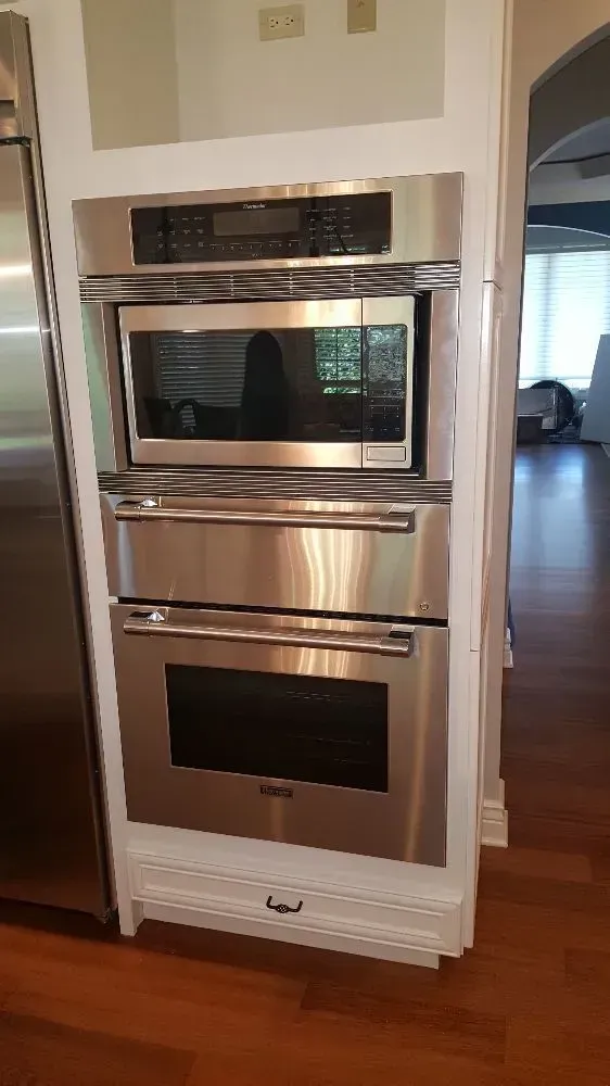 Stainless steel oven, microwave, and control panel built into a white cabinet in a kitchen.