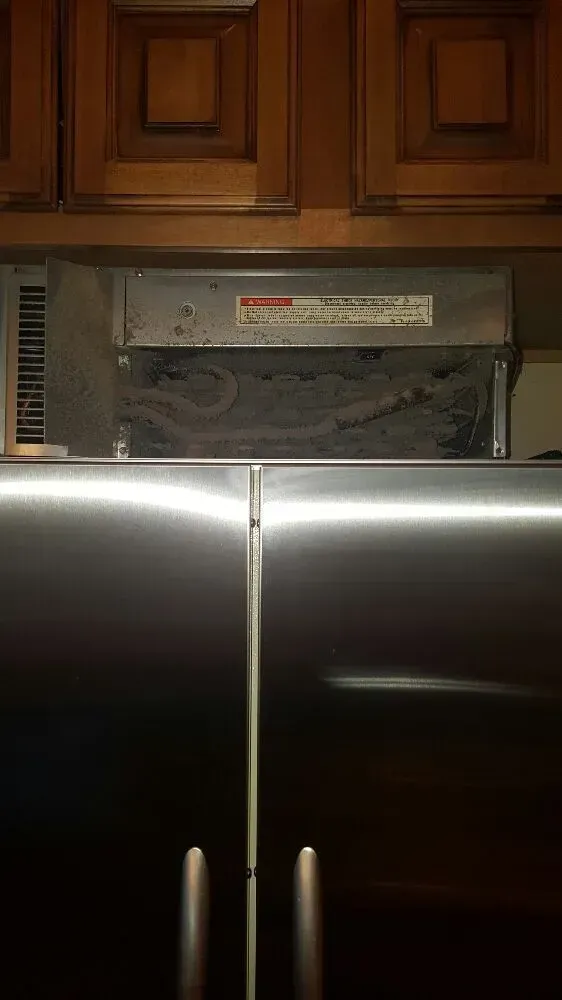 Stainless steel refrigerator with upper cabinets, vent above.