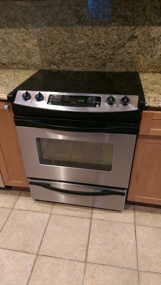 Stainless steel oven with black stovetop, sitting between light-colored cabinets, on a tiled floor.