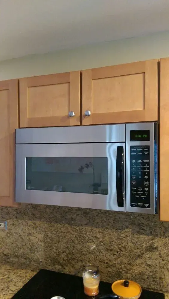 Stainless steel microwave mounted under light wood cabinets in a kitchen.