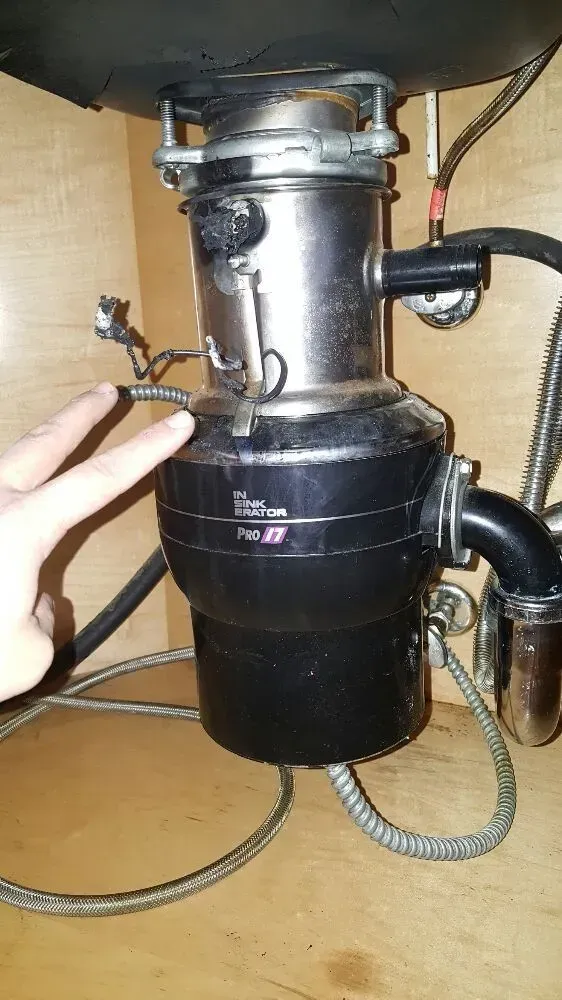 A person points to a black and silver garbage disposal unit under a kitchen sink.