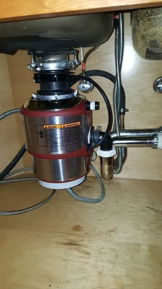 Garbage disposal under a kitchen sink with pipes and connections.