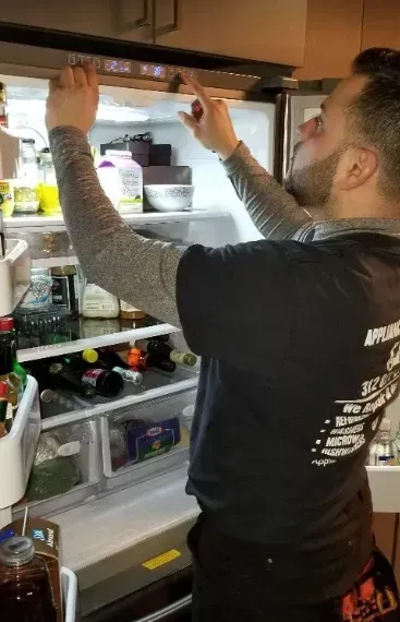 Man reaching into a refrigerator, pointing at the temperature display, with food visible inside.