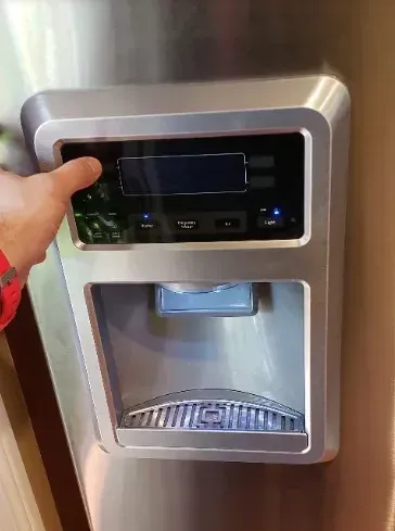 Person's finger pressing a button on a refrigerator water/ice dispenser. Stainless steel. Blue display and lights.