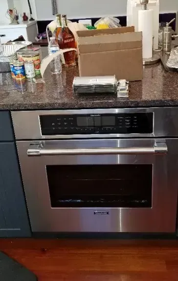 Stainless steel oven in a kitchen with granite countertop. Canned goods and liquor are visible on the countertop.