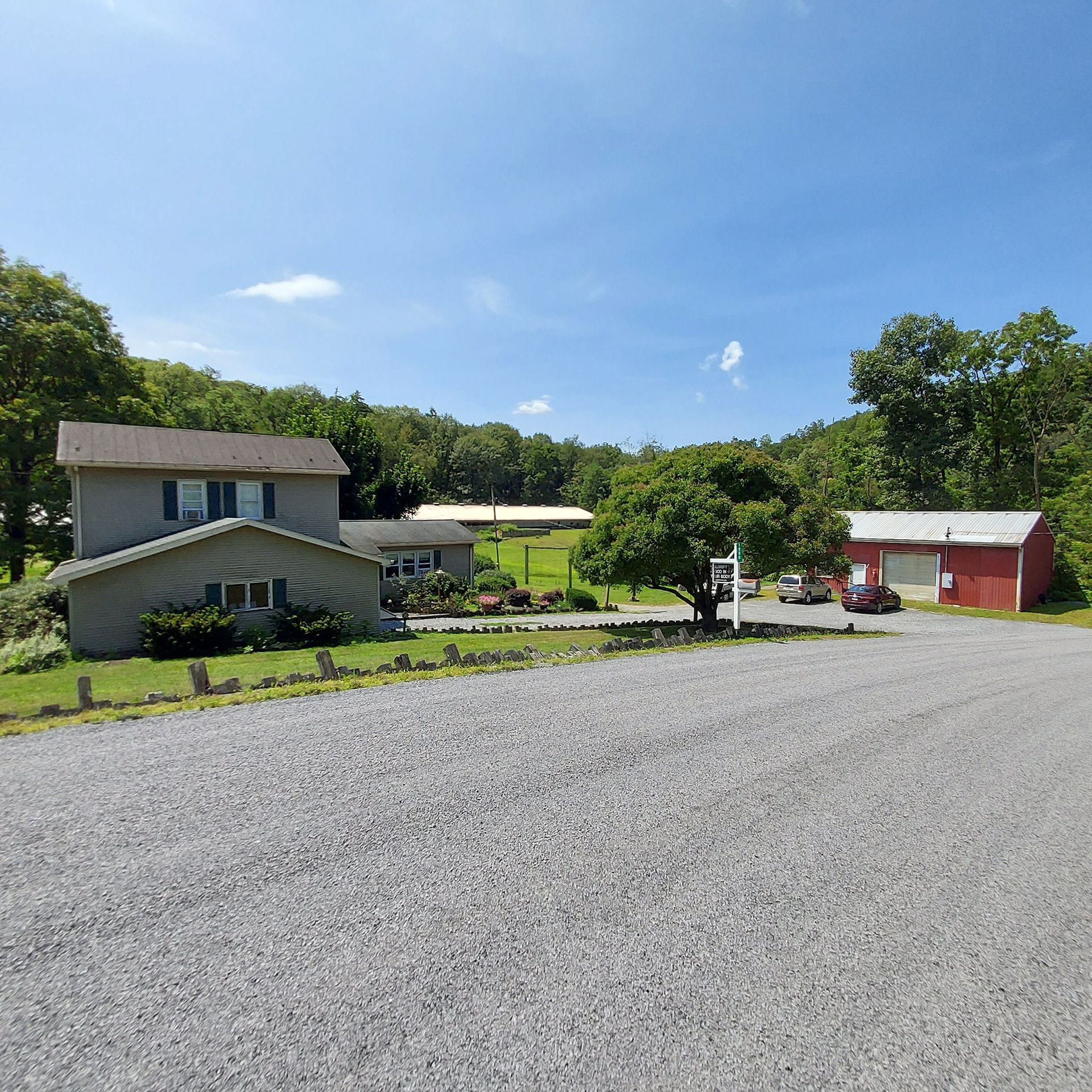 A gravel driveway leading to a house and a red barn