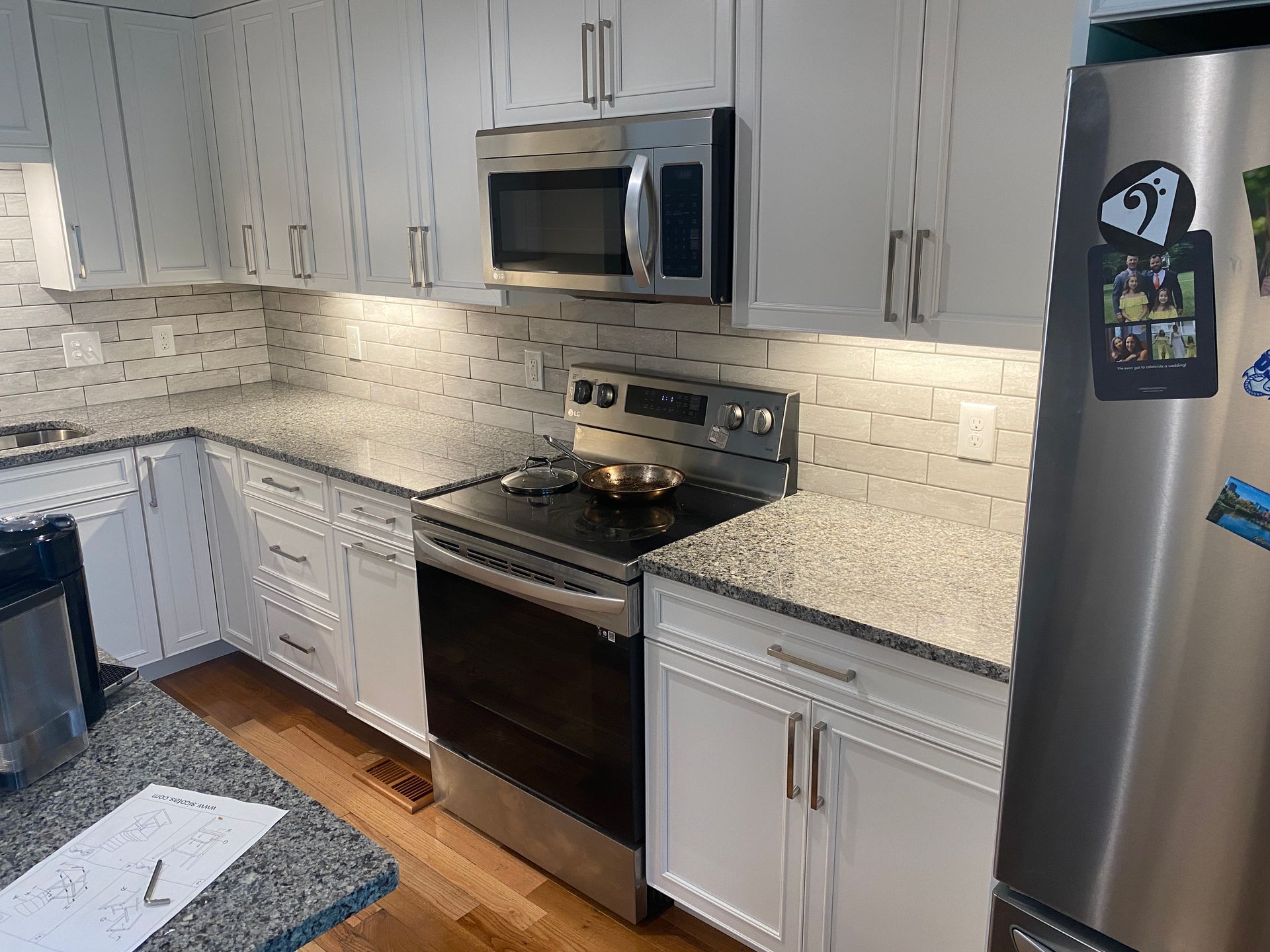 A kitchen with white cabinets , stainless steel appliances , granite counter tops and a stainless steel refrigerator.