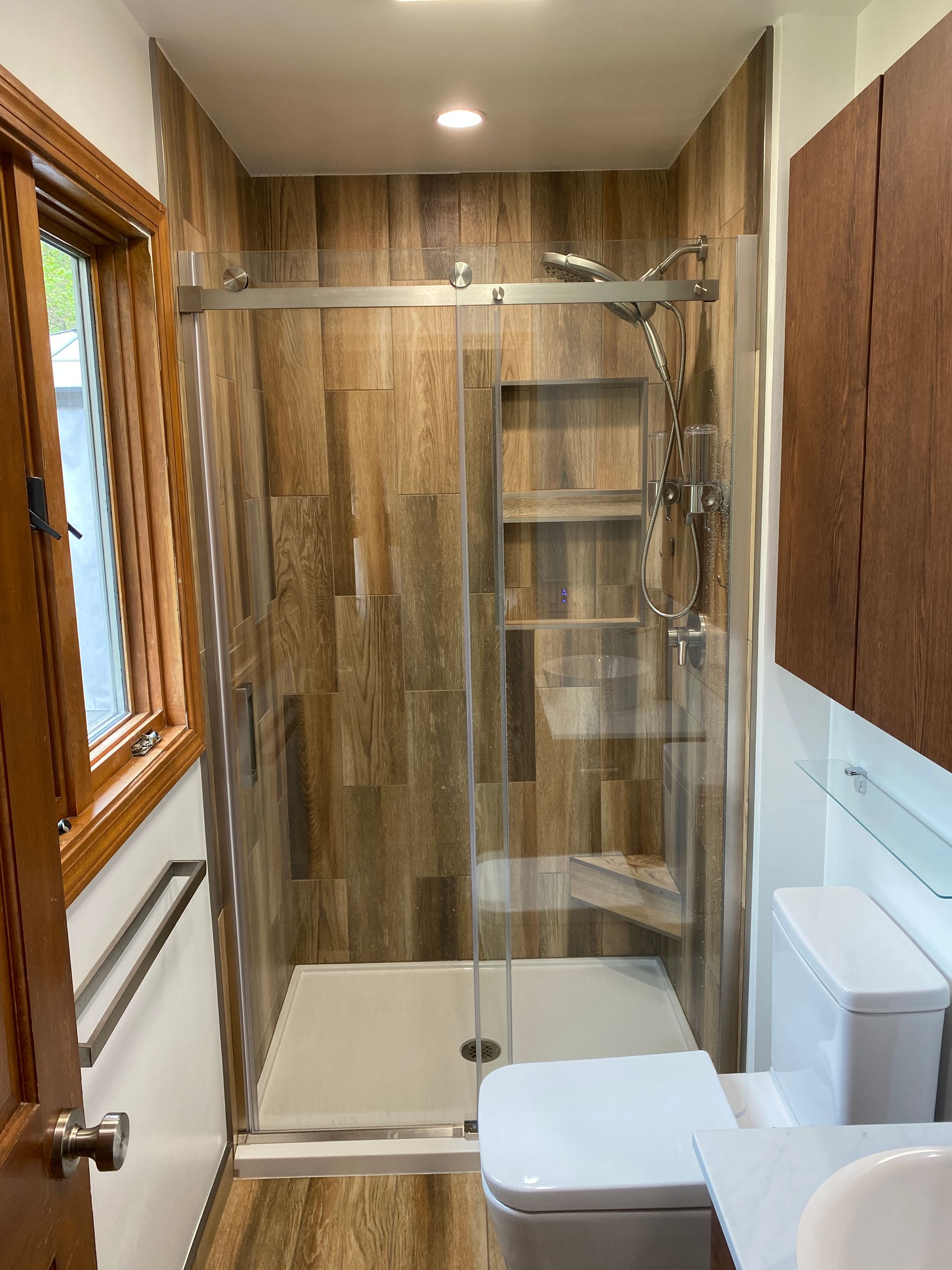 A bathroom with a sliding glass shower door , toilet , sink and window.