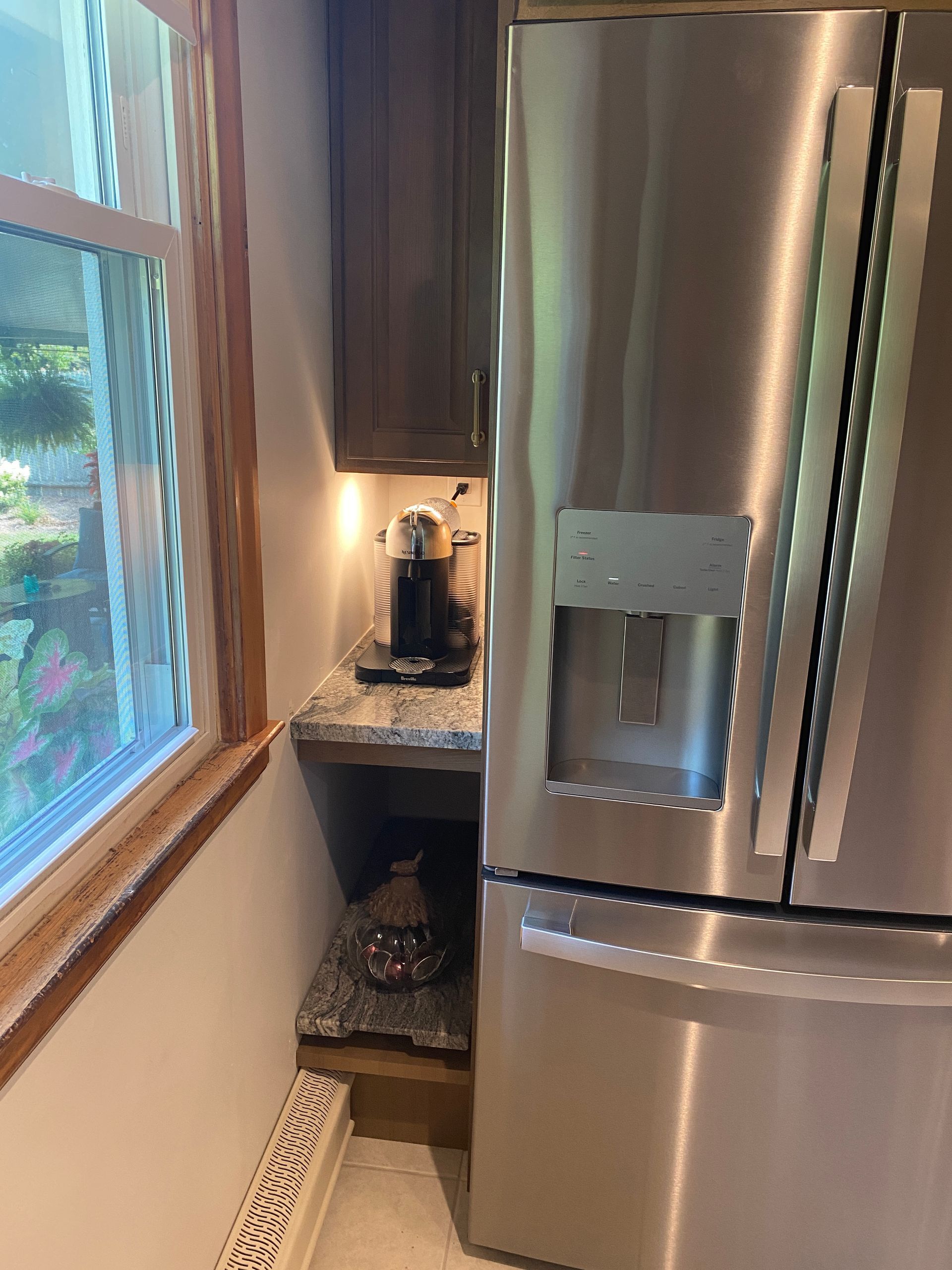 A stainless steel refrigerator is in a kitchen next to a window.