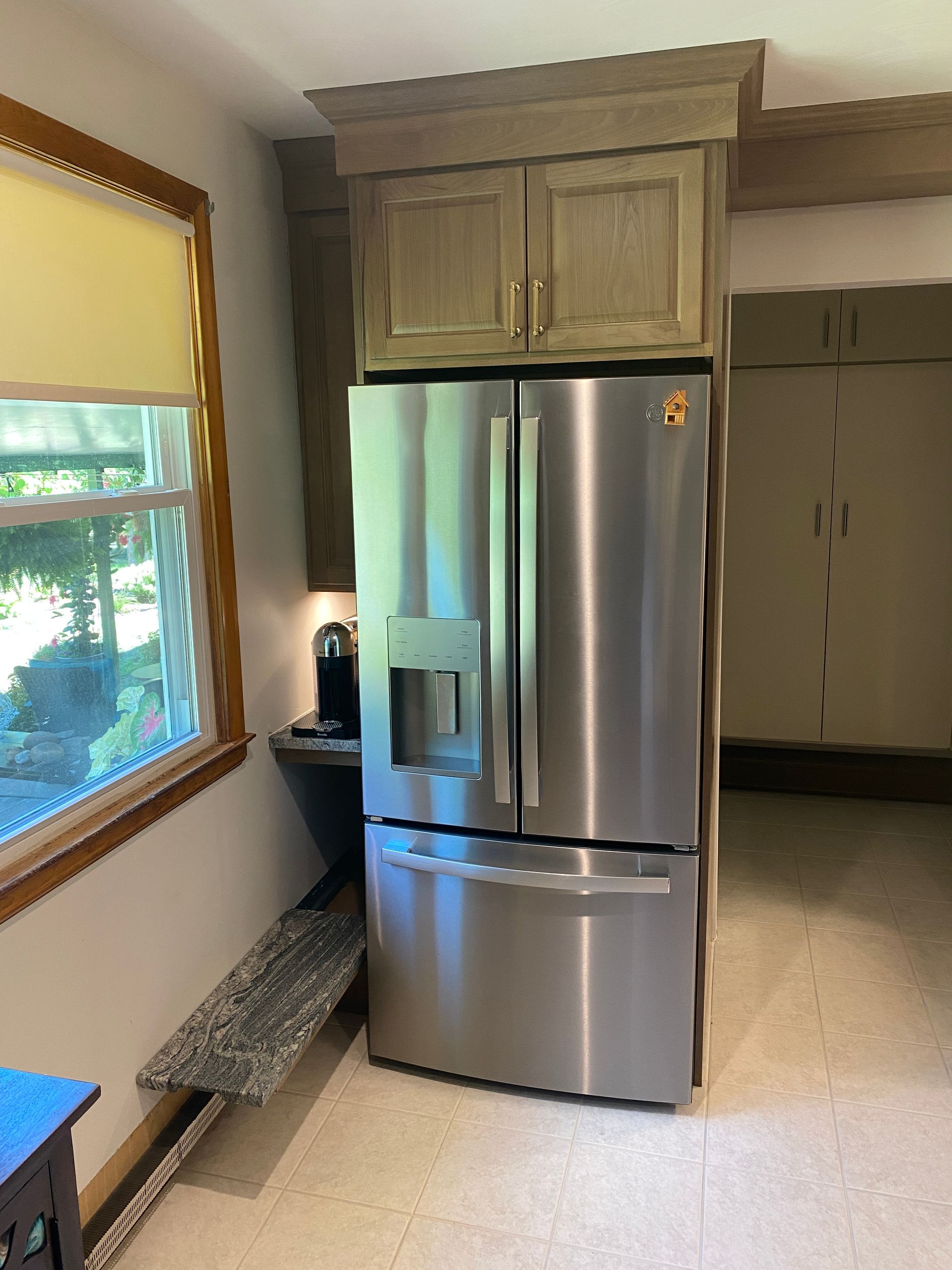 A stainless steel refrigerator in a kitchen next to a window