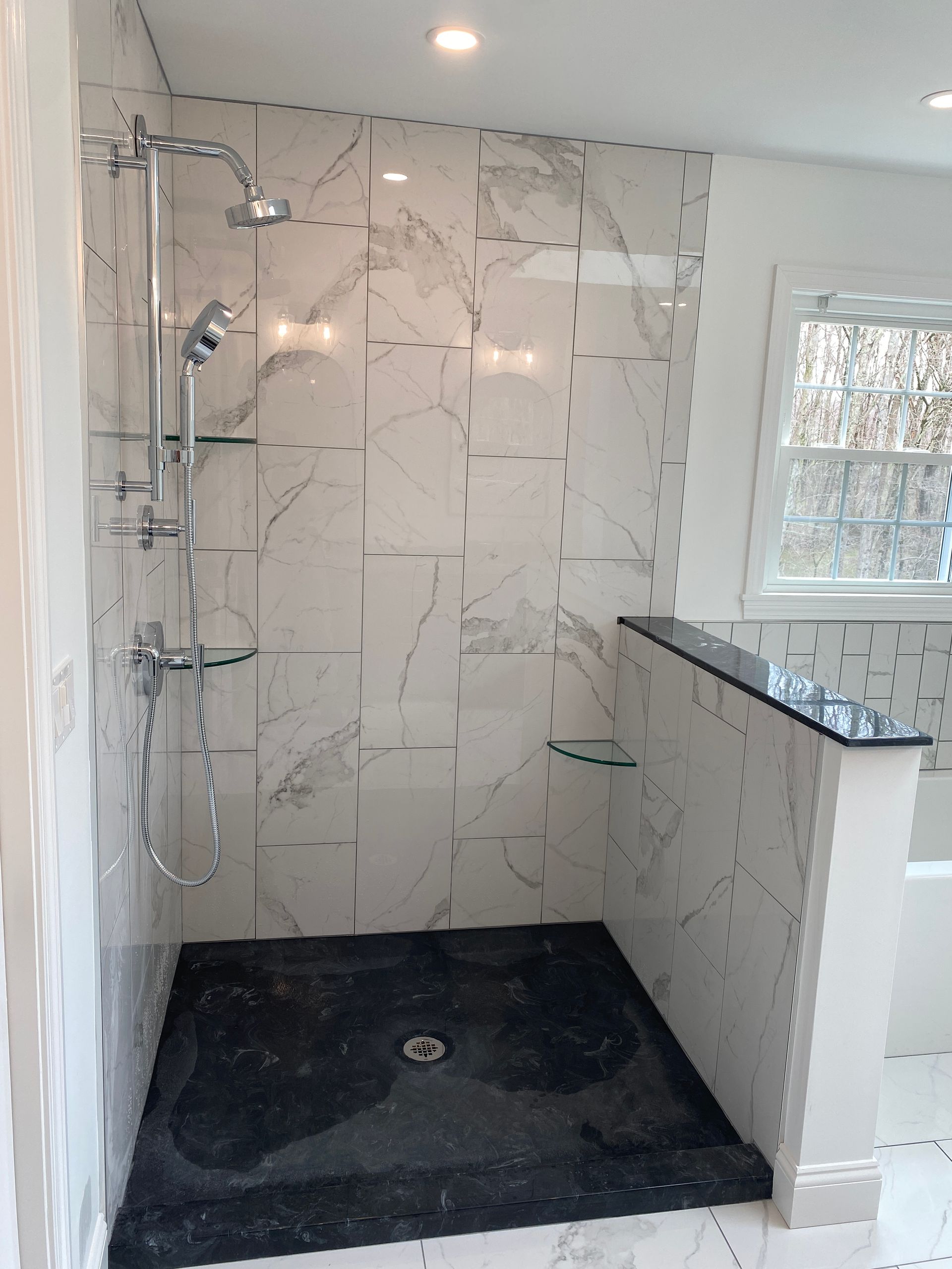A walk in shower with marble tiles and a black floor