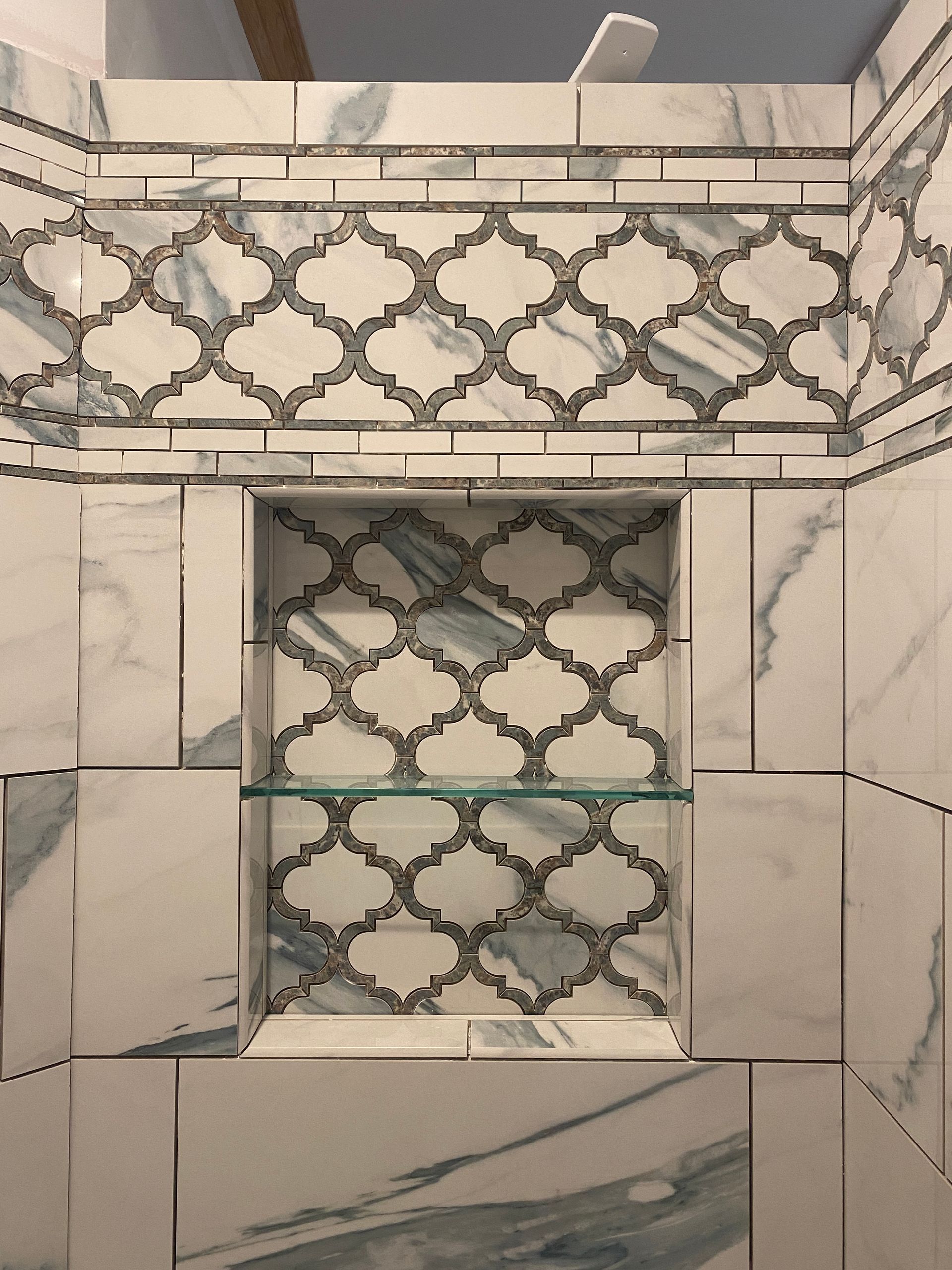 A shower niche with a glass shelf in a bathroom with marble tiles.