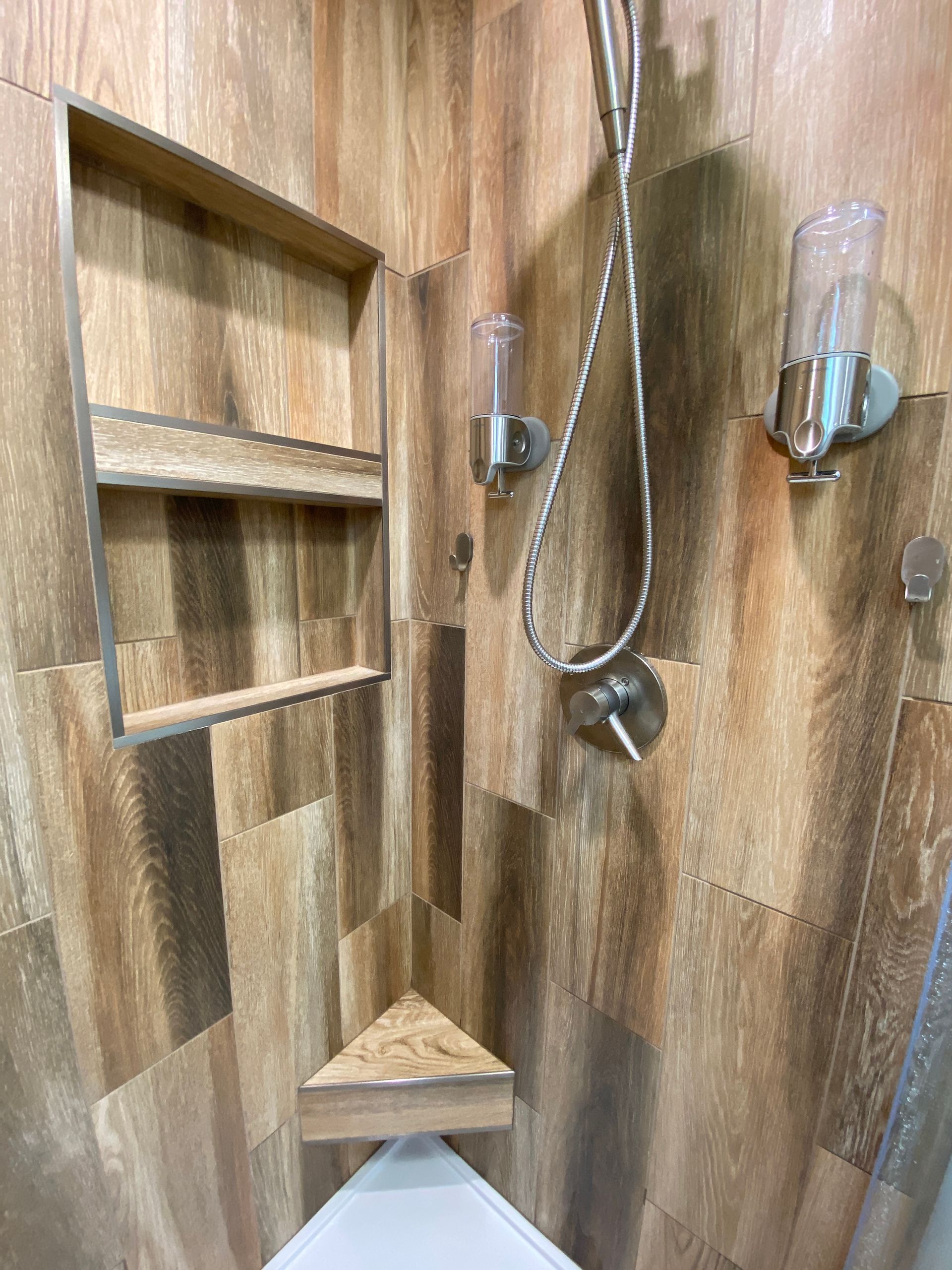 There is a shower with a wooden wall and a corner shelf.