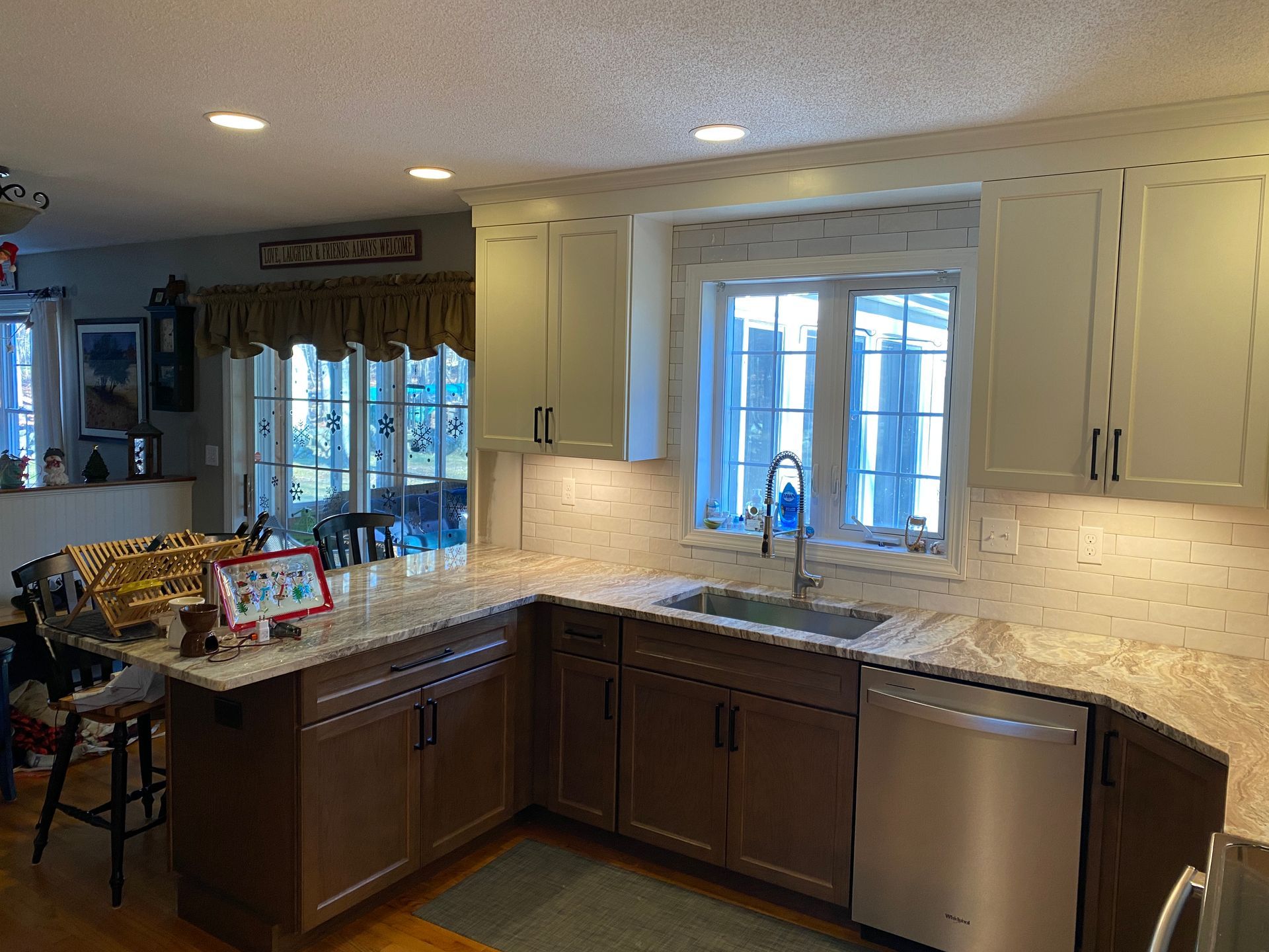 A kitchen with white cabinets , a sink , a dishwasher , and a window.