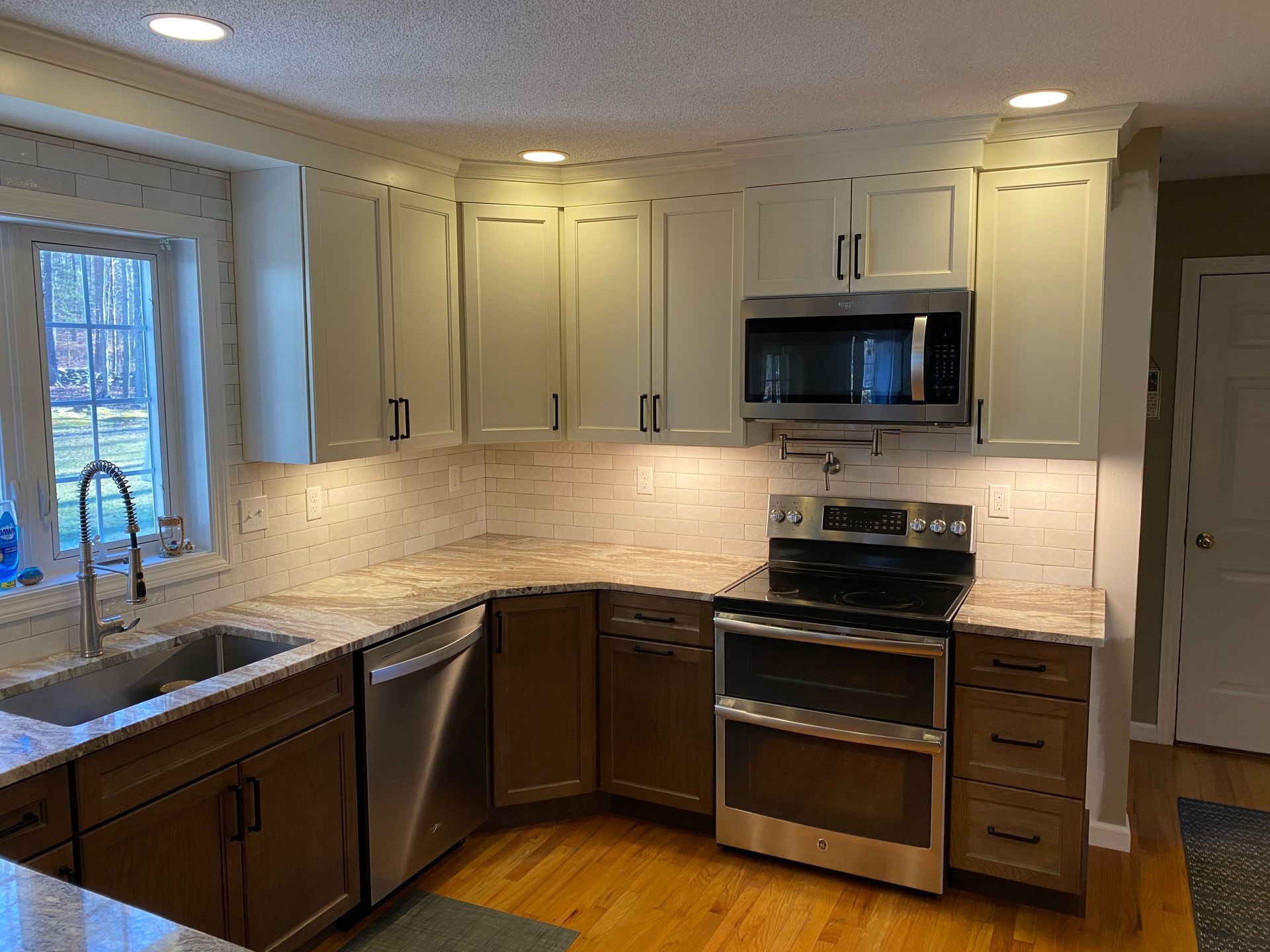 A kitchen with white cabinets , stainless steel appliances , a sink , and a window.