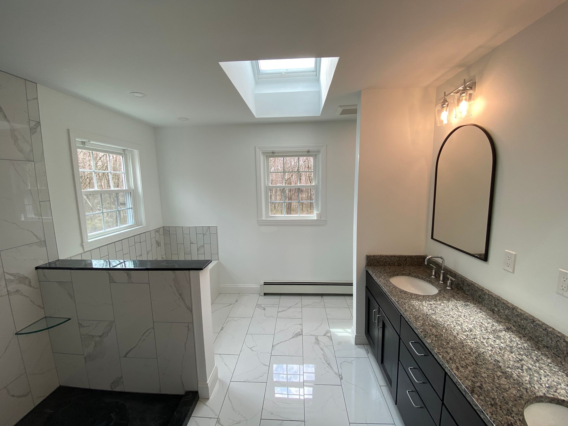 A bathroom with two sinks , a shower , and a skylight.