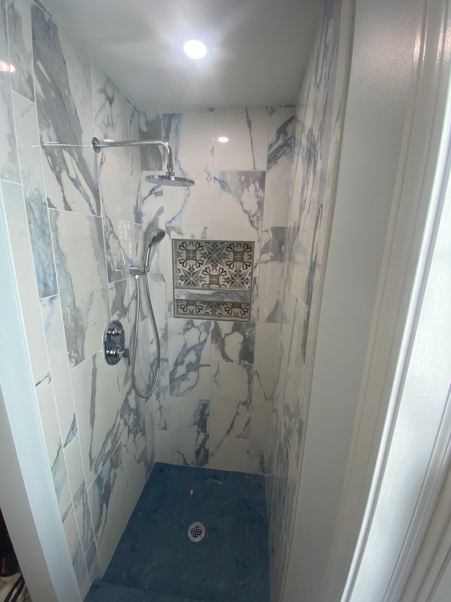 A shower stall with marble walls and a blue tile floor.