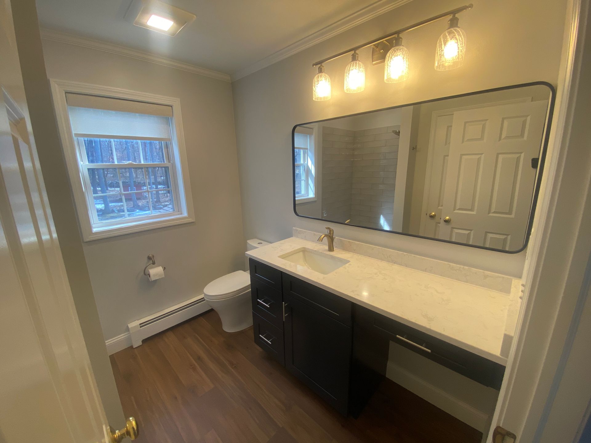 A bathroom with a toilet , sink , mirror and window.