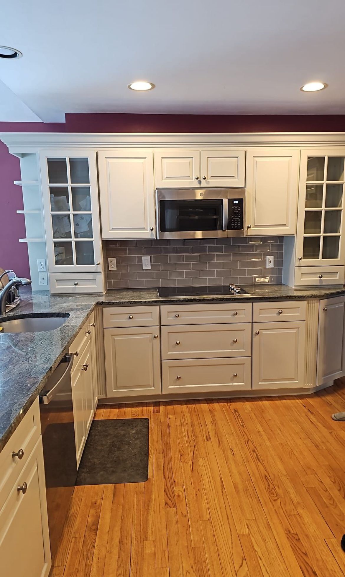 A kitchen with white cabinets , granite counter tops , and stainless steel appliances.