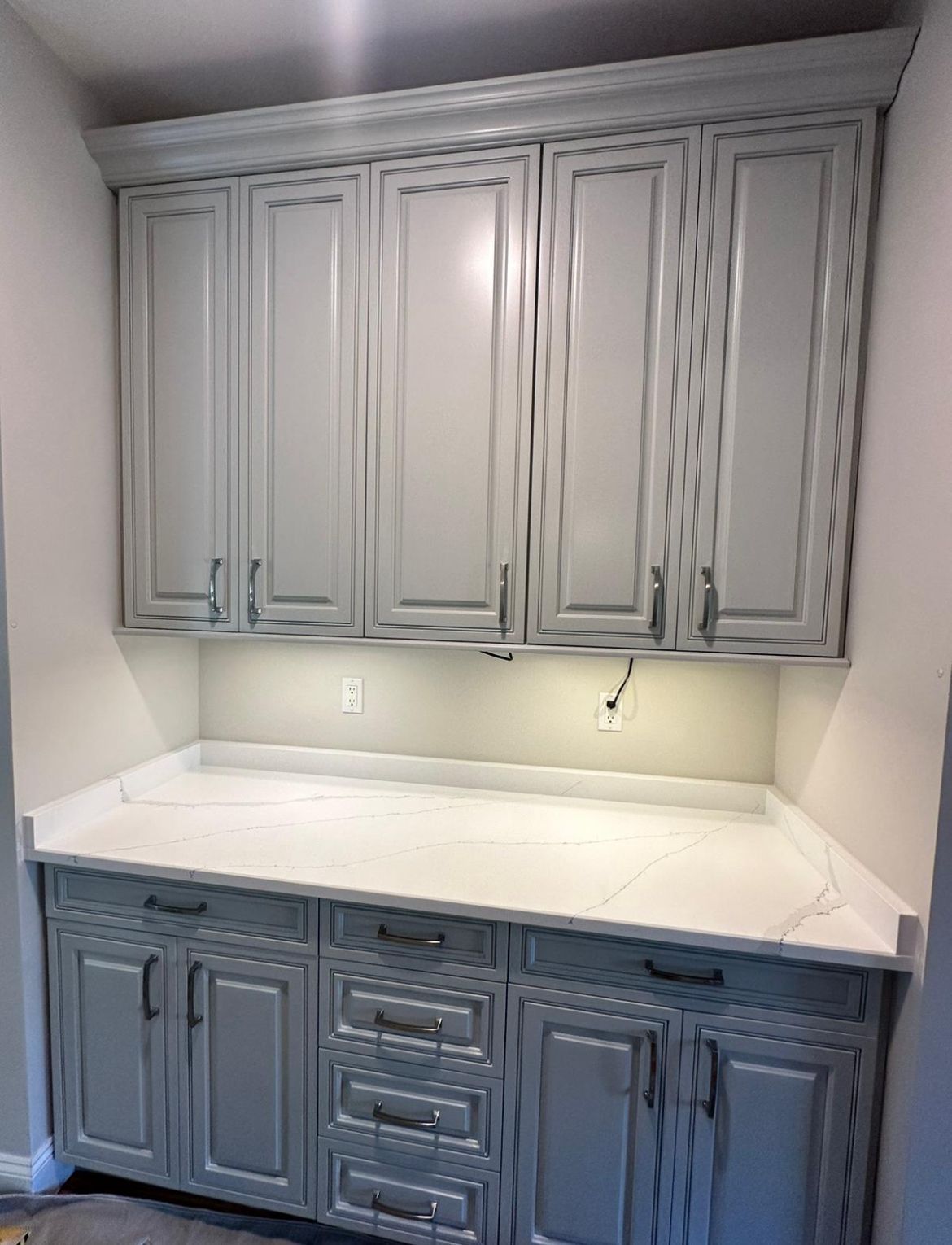 A kitchen with gray cabinets and white counter tops.