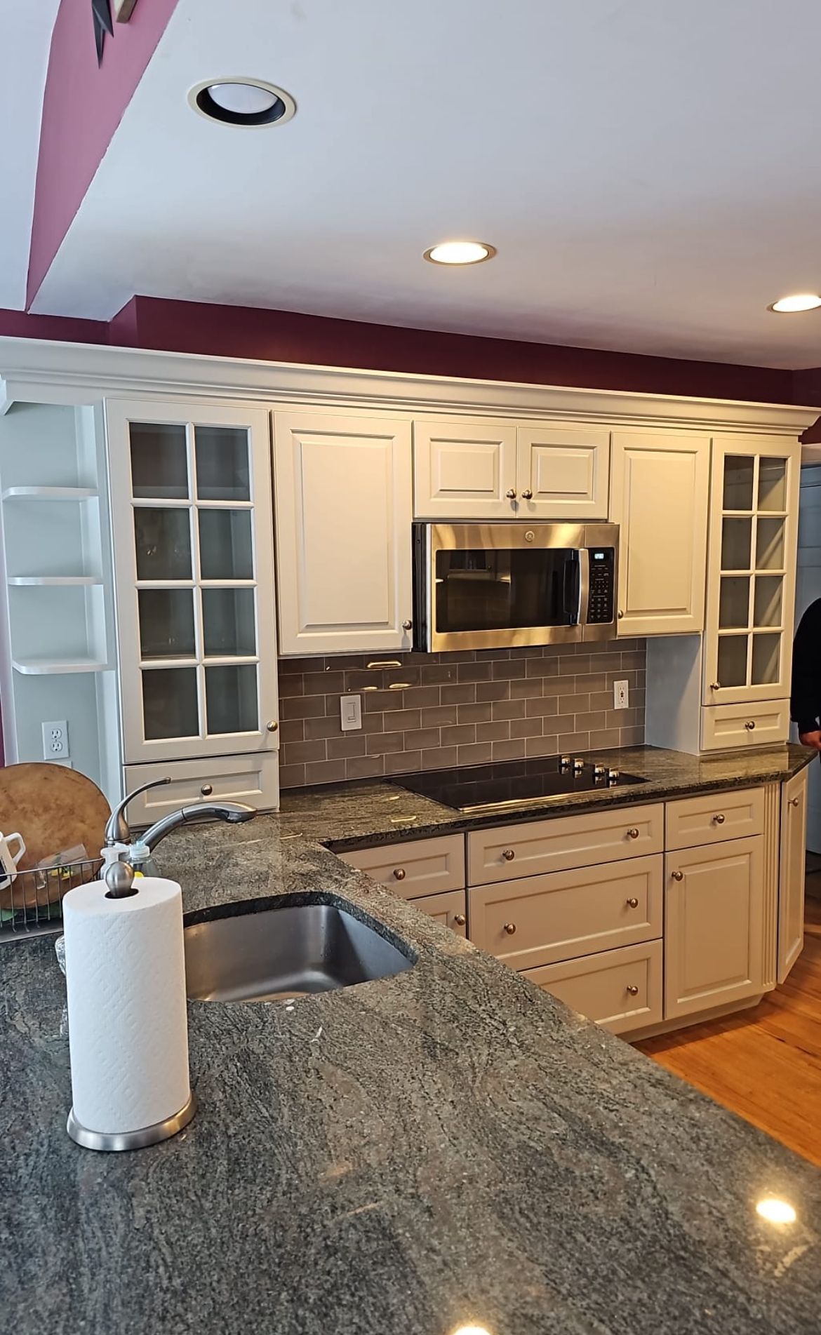 A kitchen with white cabinets , granite counter tops , stainless steel appliances and a paper towel holder.