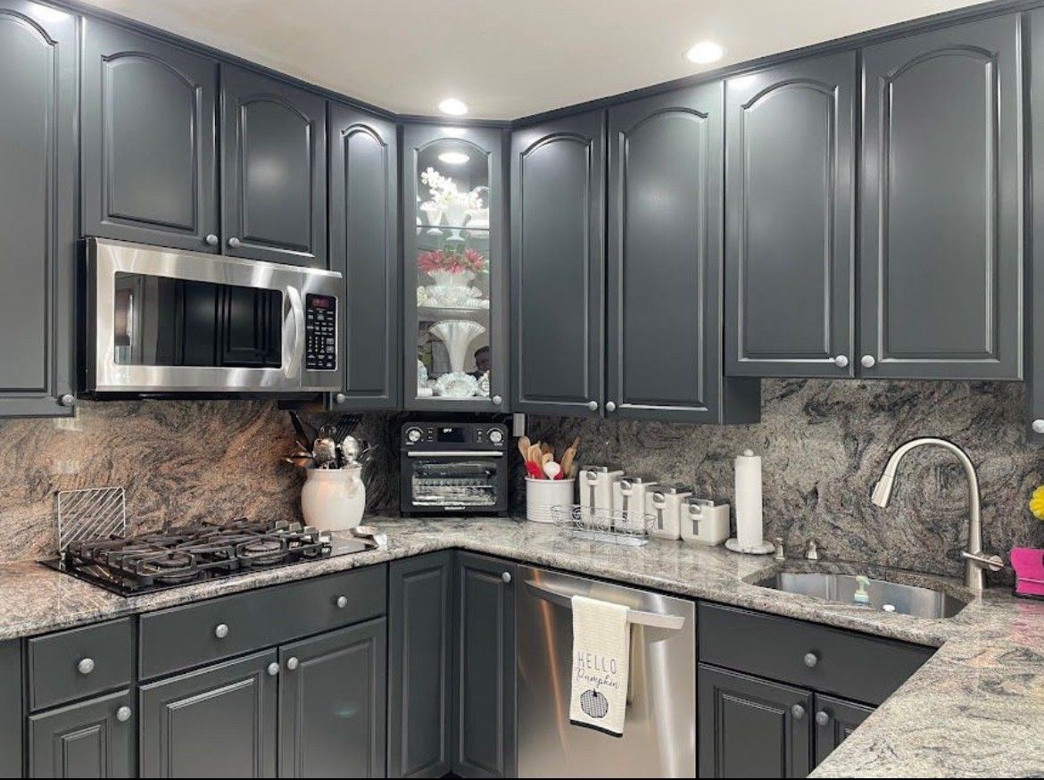A kitchen with gray cabinets , granite counter tops , stainless steel appliances and a microwave.