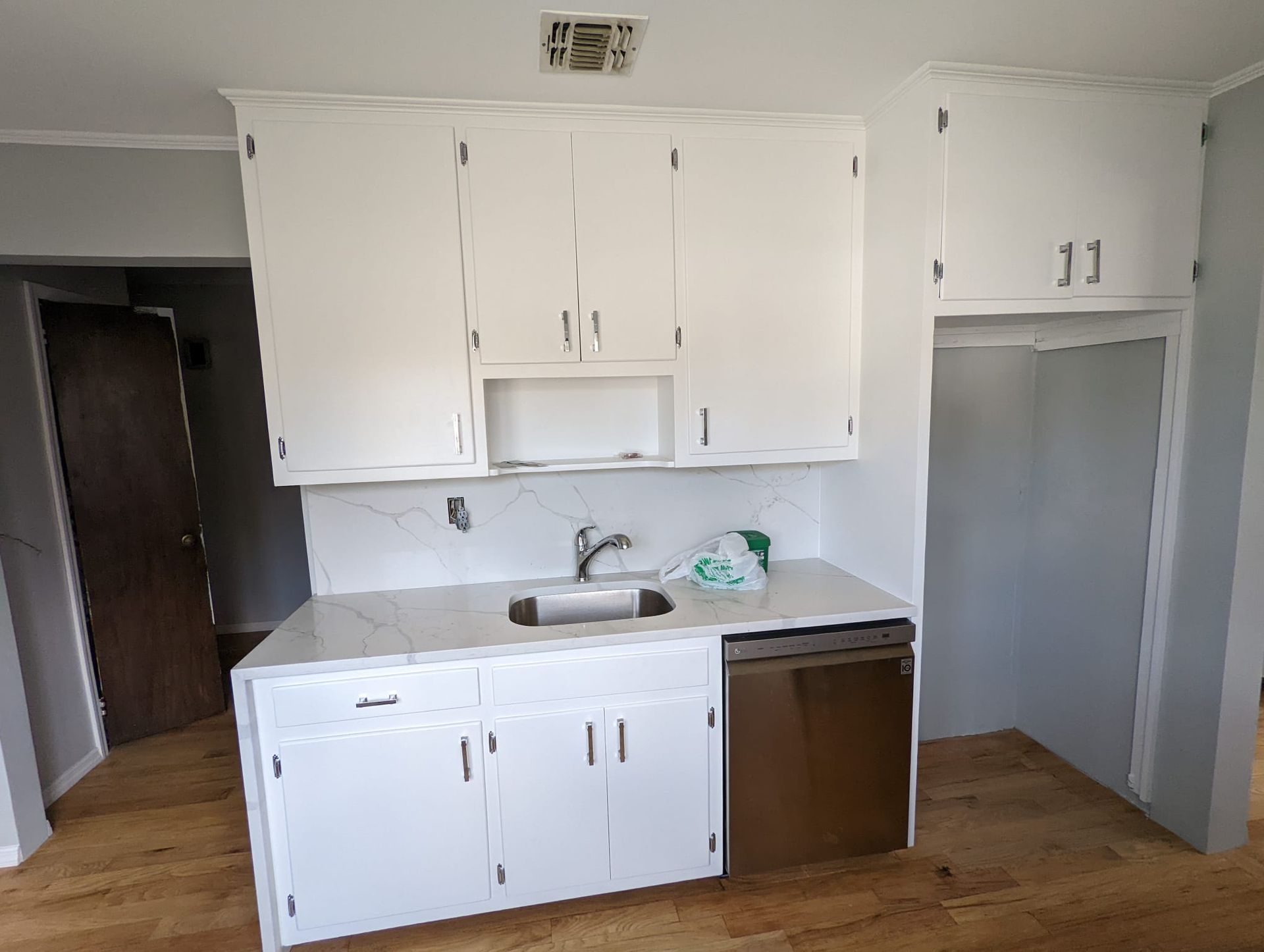 A kitchen with white cabinets , a sink , and a dishwasher.