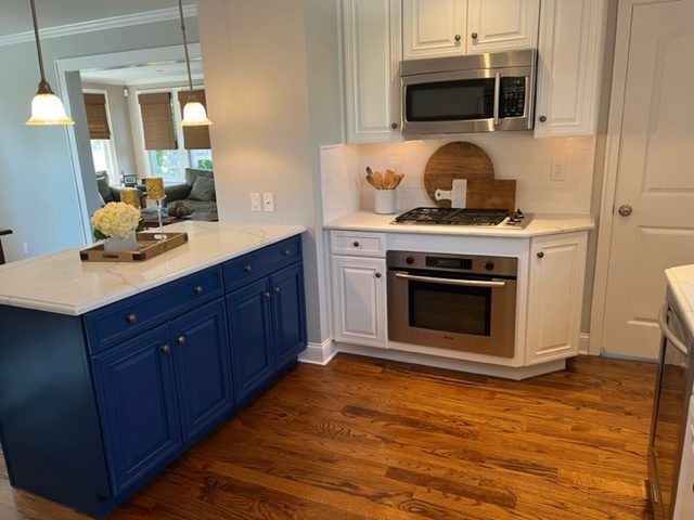 A kitchen with blue cabinets, white cabinets, stainless steel appliances and a microwave.