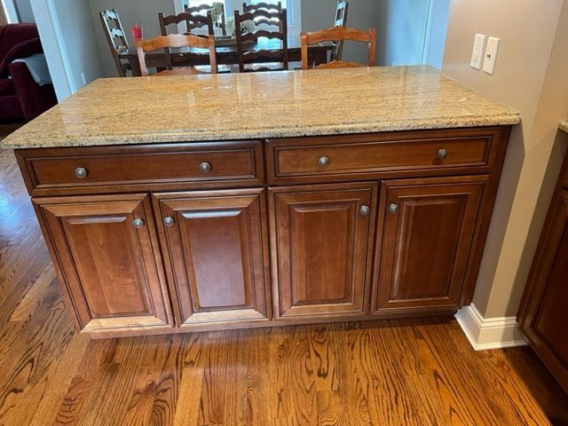 A kitchen island with wooden cabinets and a granite counter top.