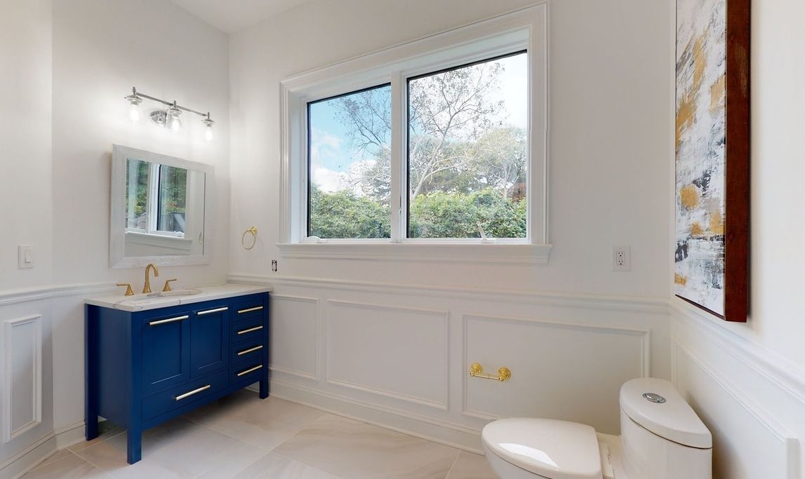 A bathroom with a toilet, sink, mirror and window.