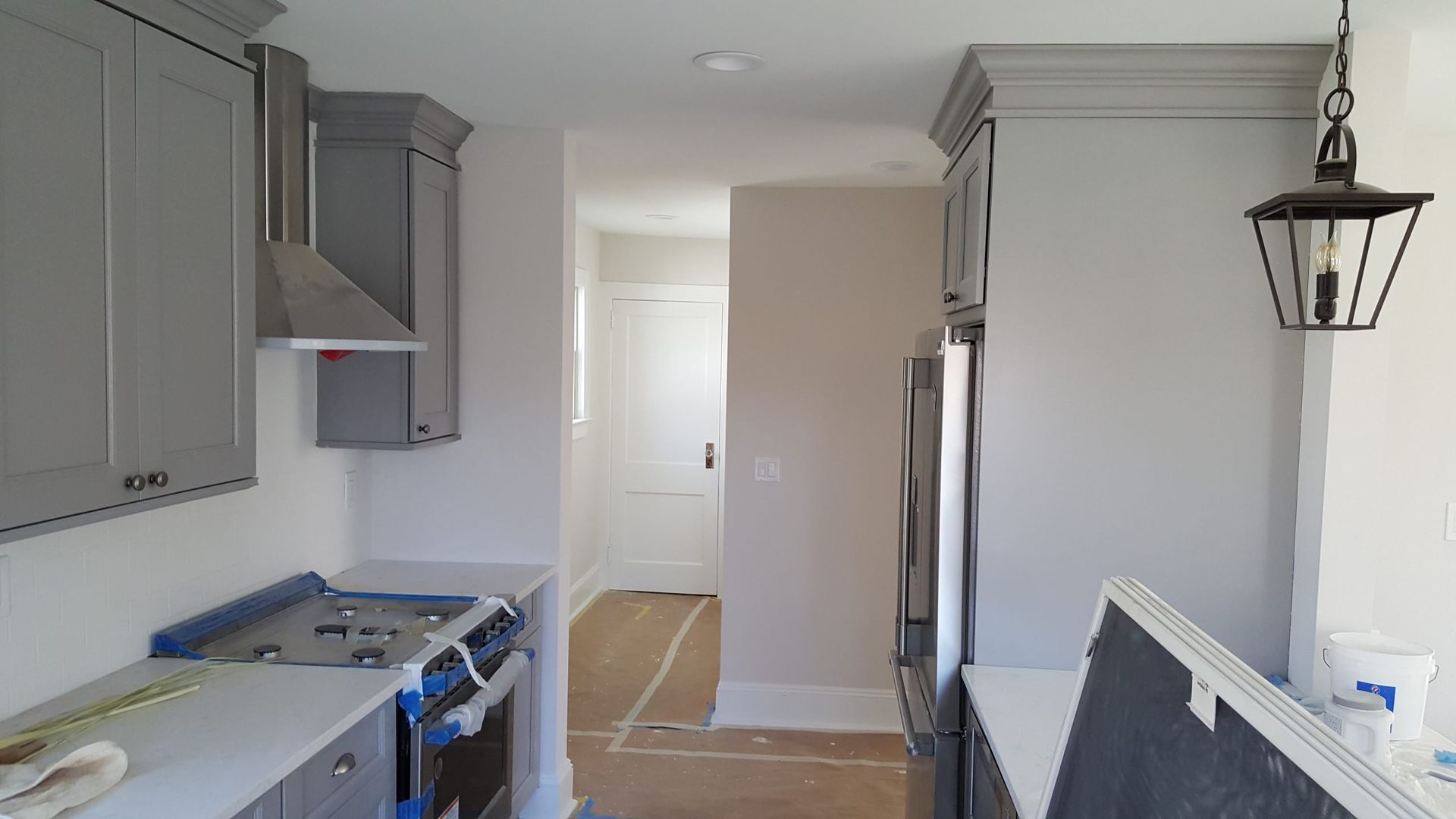 A kitchen with gray cabinets, a stove, a refrigerator and a lantern hanging from the ceiling.