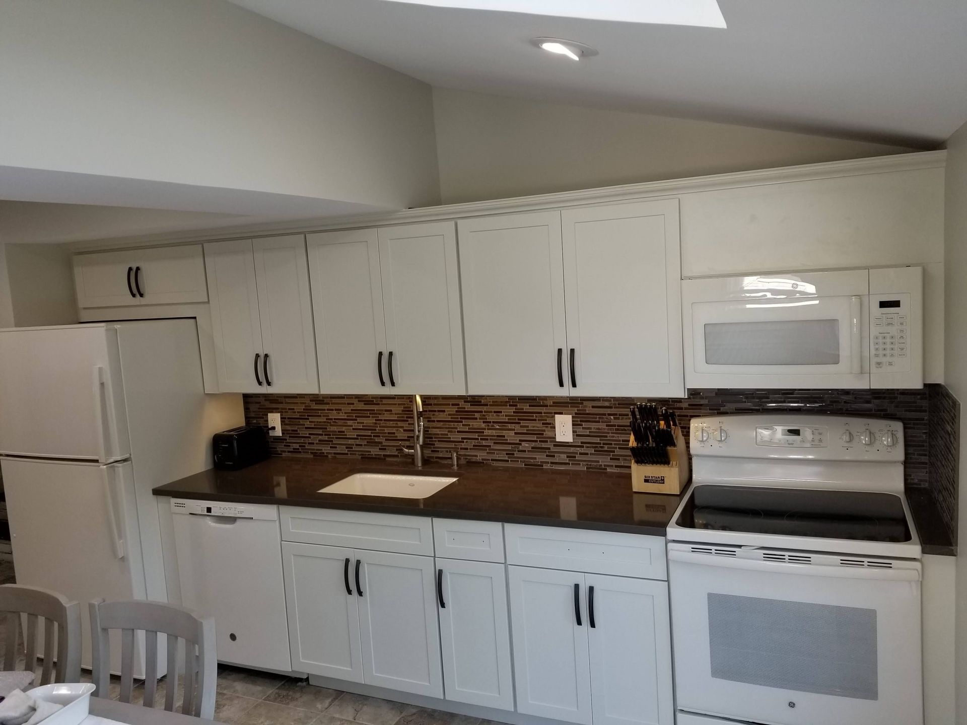 A kitchen with white cabinets, a stove, microwave and refrigerator.